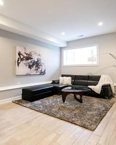 Finished basement with black sectional sofa, white brick fireplace, wall-mounted TV, and abstract artwork