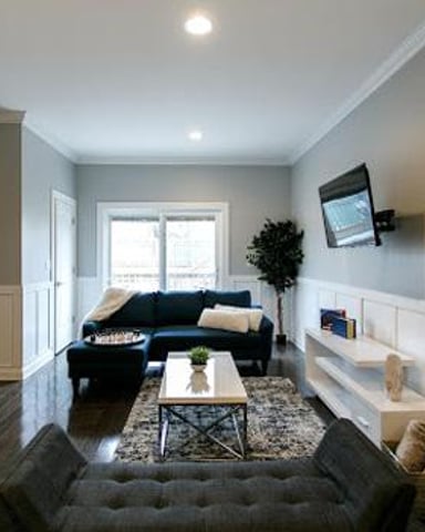 Modern living room with dark blue sofa, white shiplap walls, wood flooring, and wall-mounted TV