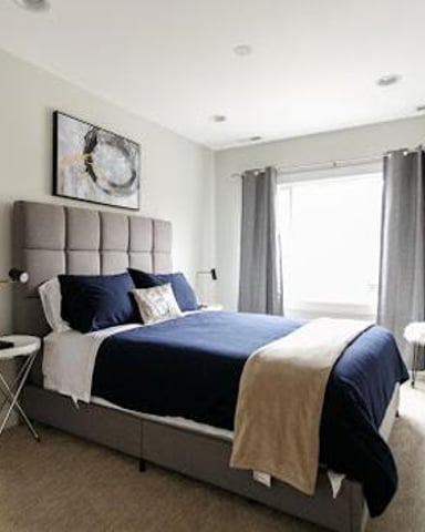 Bedroom with upholstered headboard, navy bedding, large windows with gray curtains, and modern nightstands