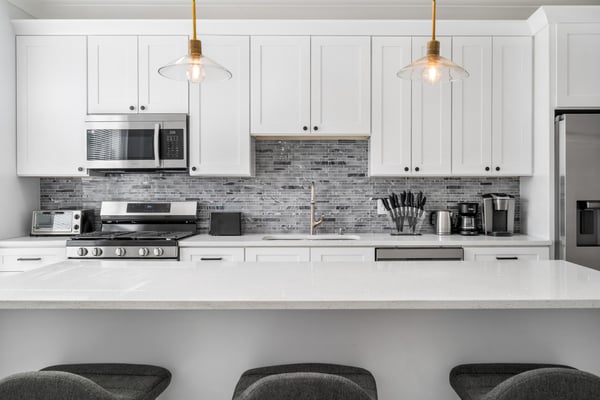 Modern kitchen with white cabinetry, gray subway tile backsplash, stainless steel appliances, and brass pendant lights over white countertop.