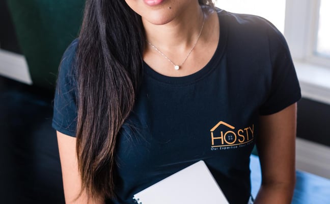 Woman in black shirt holding notebook in bright office with window behind her
